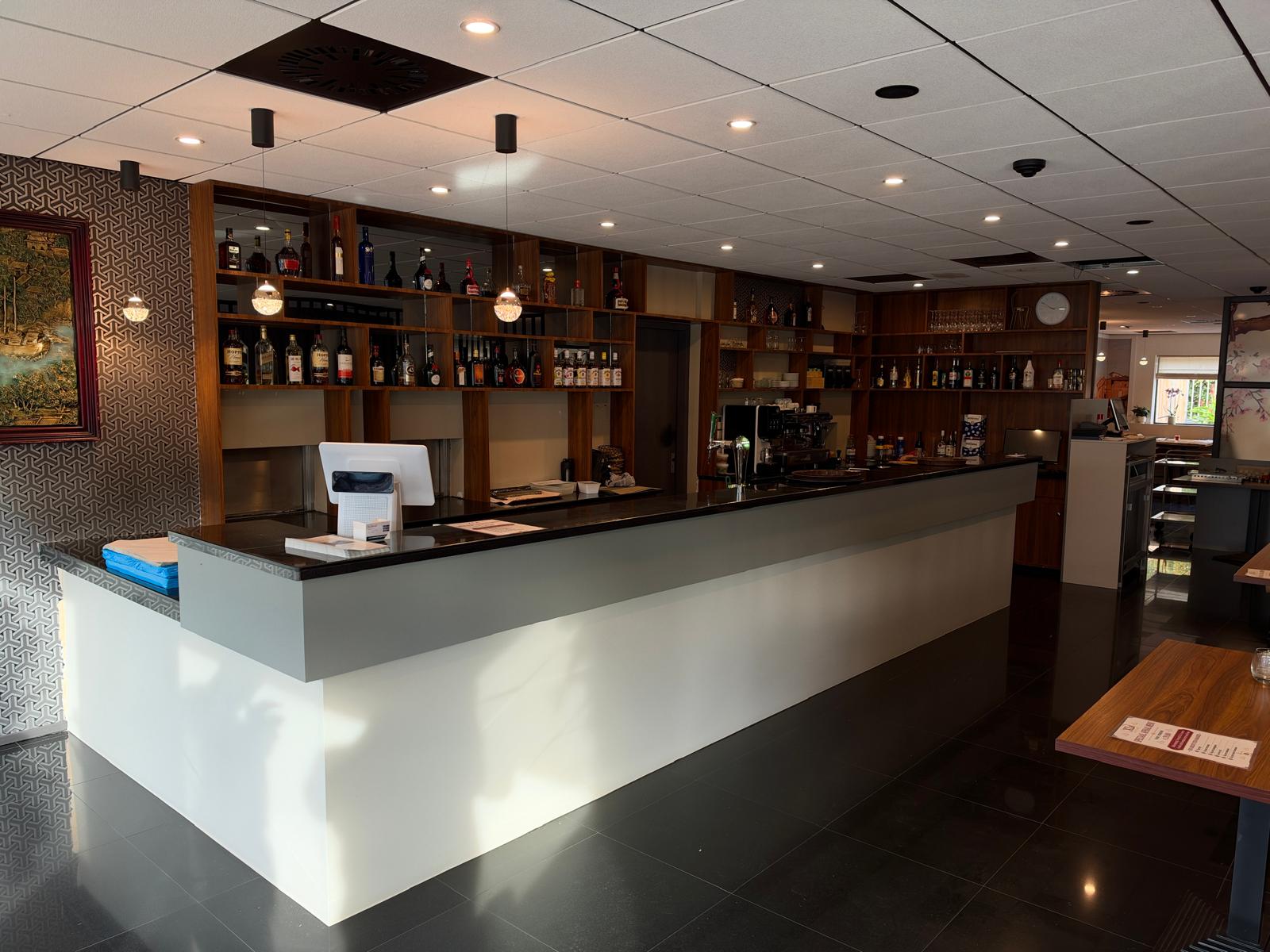 De lange bar van XL Eetcafé met houten flessenkast, hanglampen en een gouden reliëf aan de wand