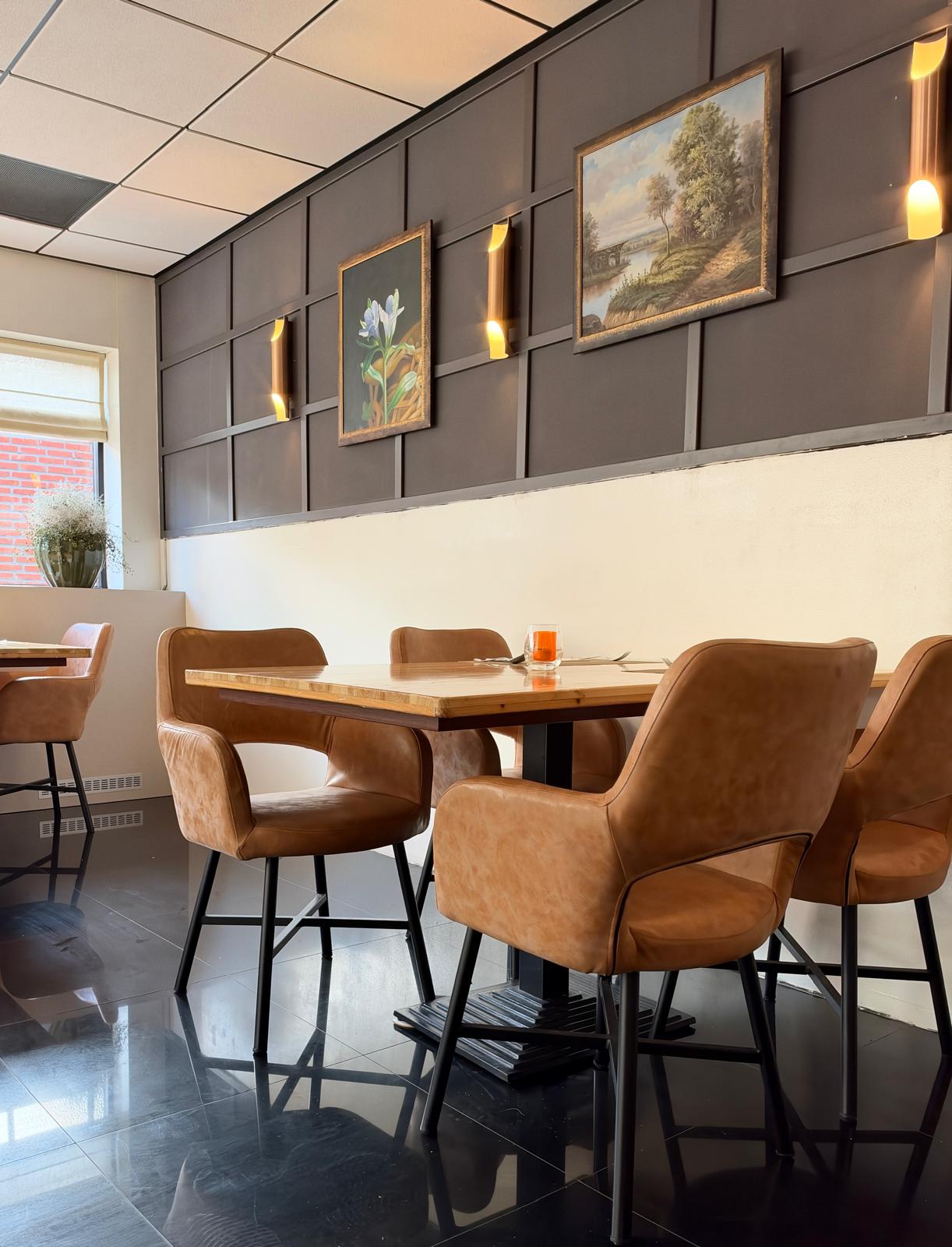 Tafel met leren stoelen voor een donkere wand met schilderijen en gouden wandlampen